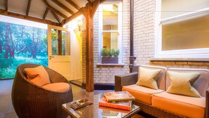 A cozy seating area with wicker furniture, a glass coffee table, and a view of a forest through a door.