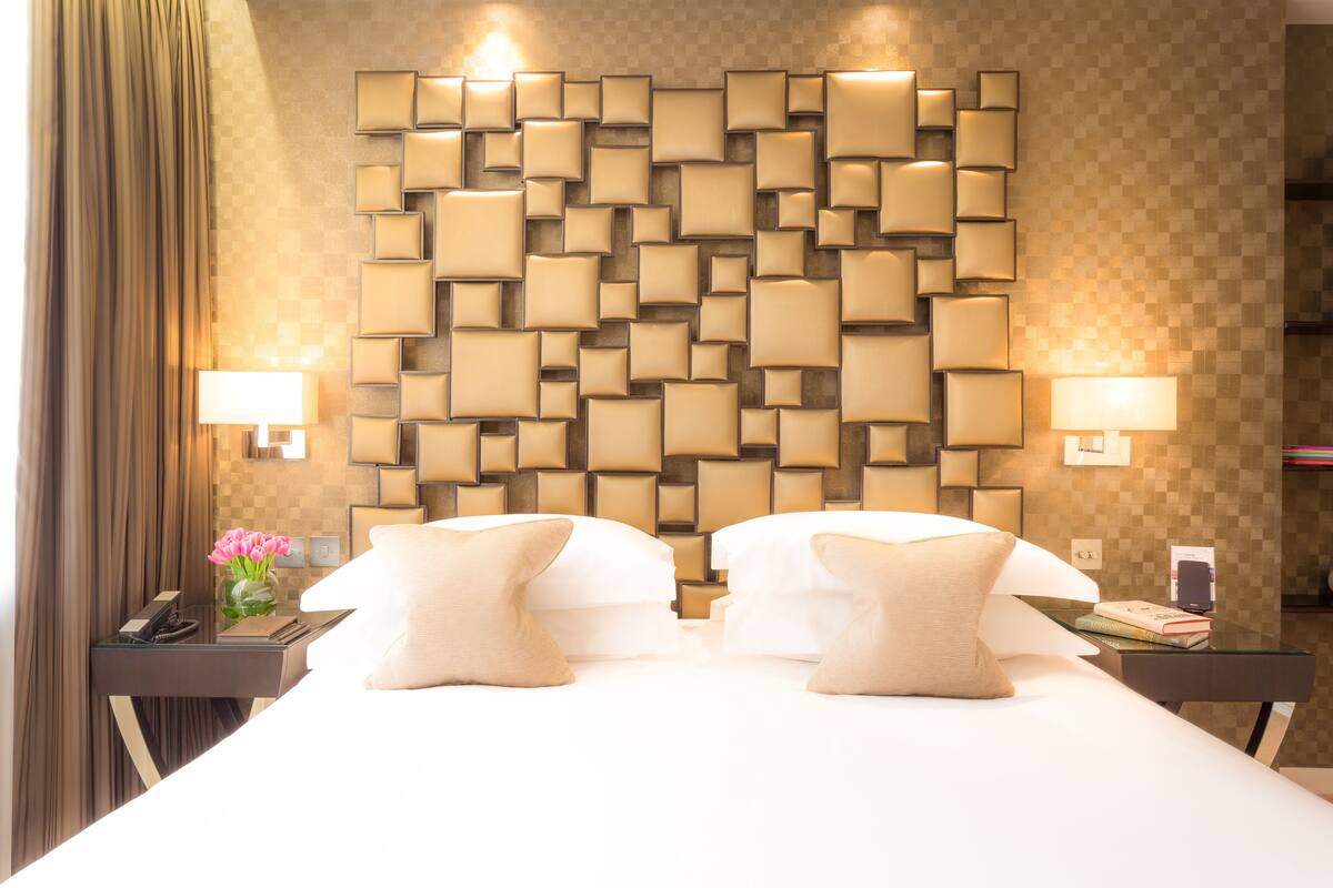 A hotel room with a large bed, two bedside tables, a wall-mounted light panel, and a curtain.