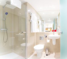 Ein modernes Badezimmer mit einer gläsernen Duschkabine, Toilette, Waschbecken und Spiegel.