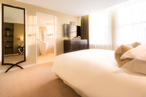 Ein Hotelzimmer mit einem großen Bett, einem Fernseher auf einem Schrank, einem Spiegel und Blick ins Badezimmer.