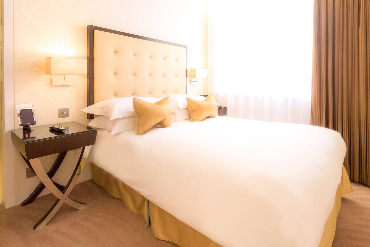 A hotel room with a large bed, a nightstand, a lamp, and a window with curtains.