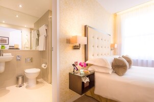 A hotel room with a bed, bedside table, nightstand, lamp, and a bathroom with a toilet, sink, and mirror.