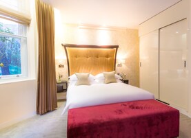 A hotel room with a large bed, a bedside table with a lamp, a window with curtains, and a wardrobe.