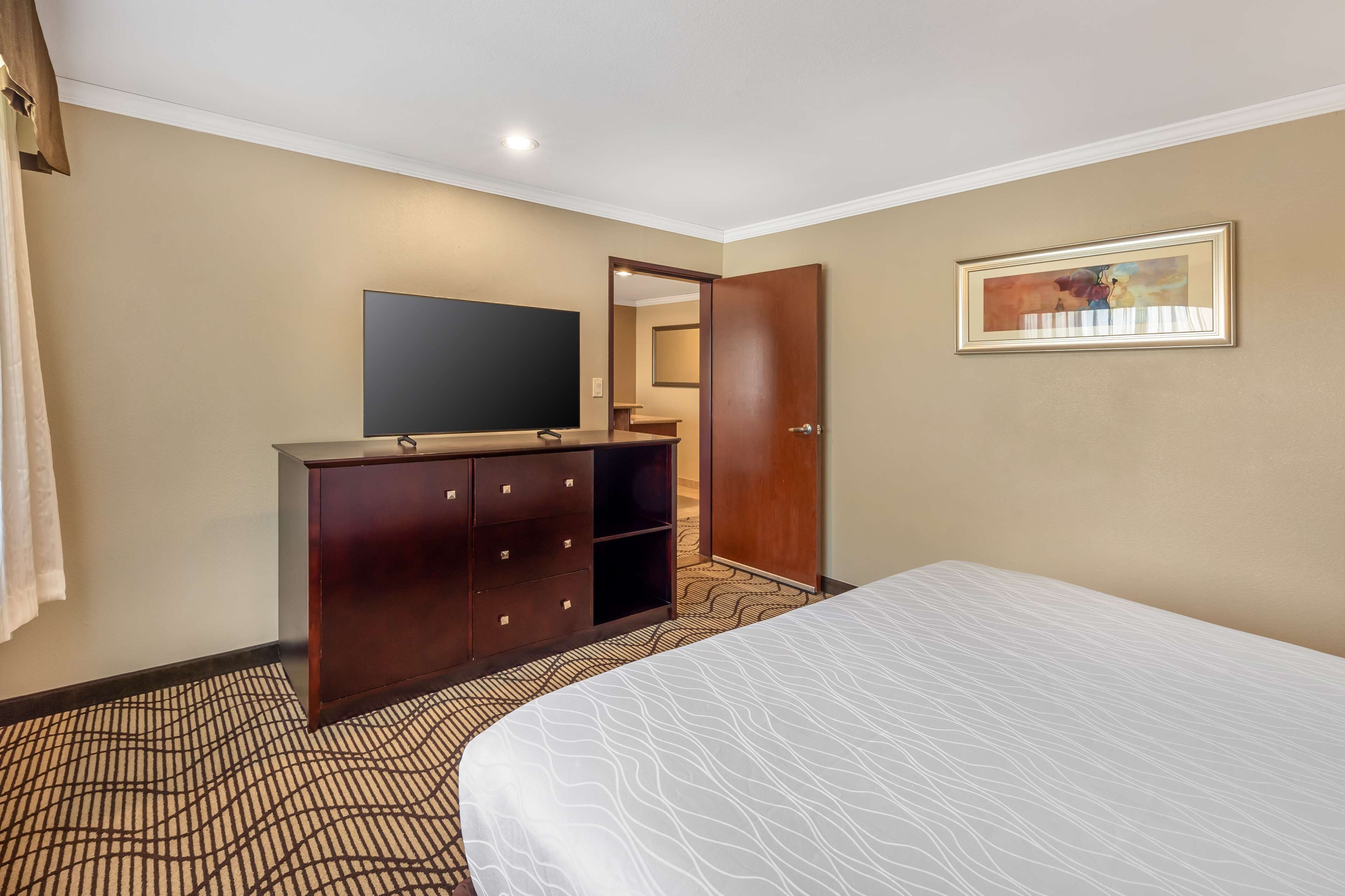 A hotel room with a bed, a dresser, a flat-screen TV, and a painting on the wall.