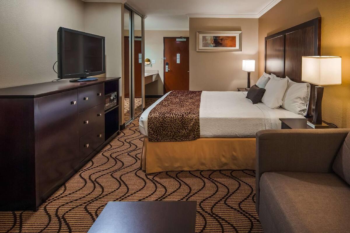 A hotel room with a bed, a TV, a desk, a lamp, and a couch.