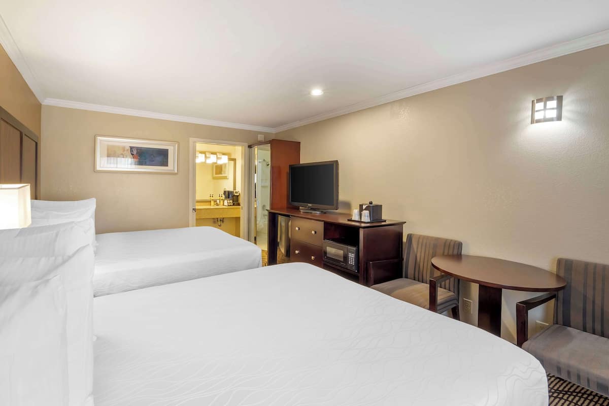A hotel room with two beds, a TV, a small table, and a seating area.