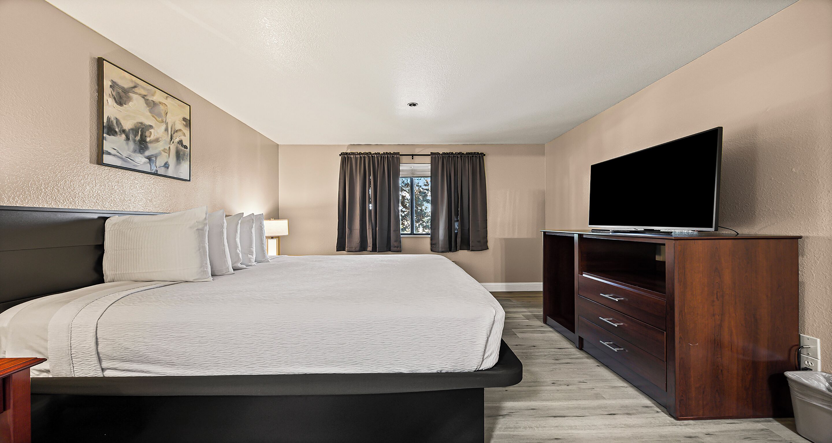Ein Hotelzimmer mit Bett, Fernseher, Holzschrank und einem Fenster mit Vorhängen.