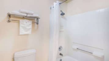 Et badeværelse med toilet, bruser med gardin og et håndklædestativ med foldede håndklæder.