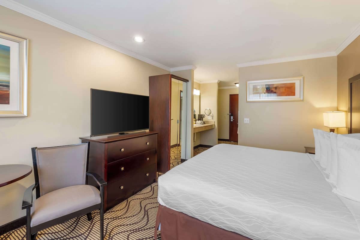 A hotel room with a bed, a TV, a desk with a chair, a dresser, and a bathroom visible through an open door.