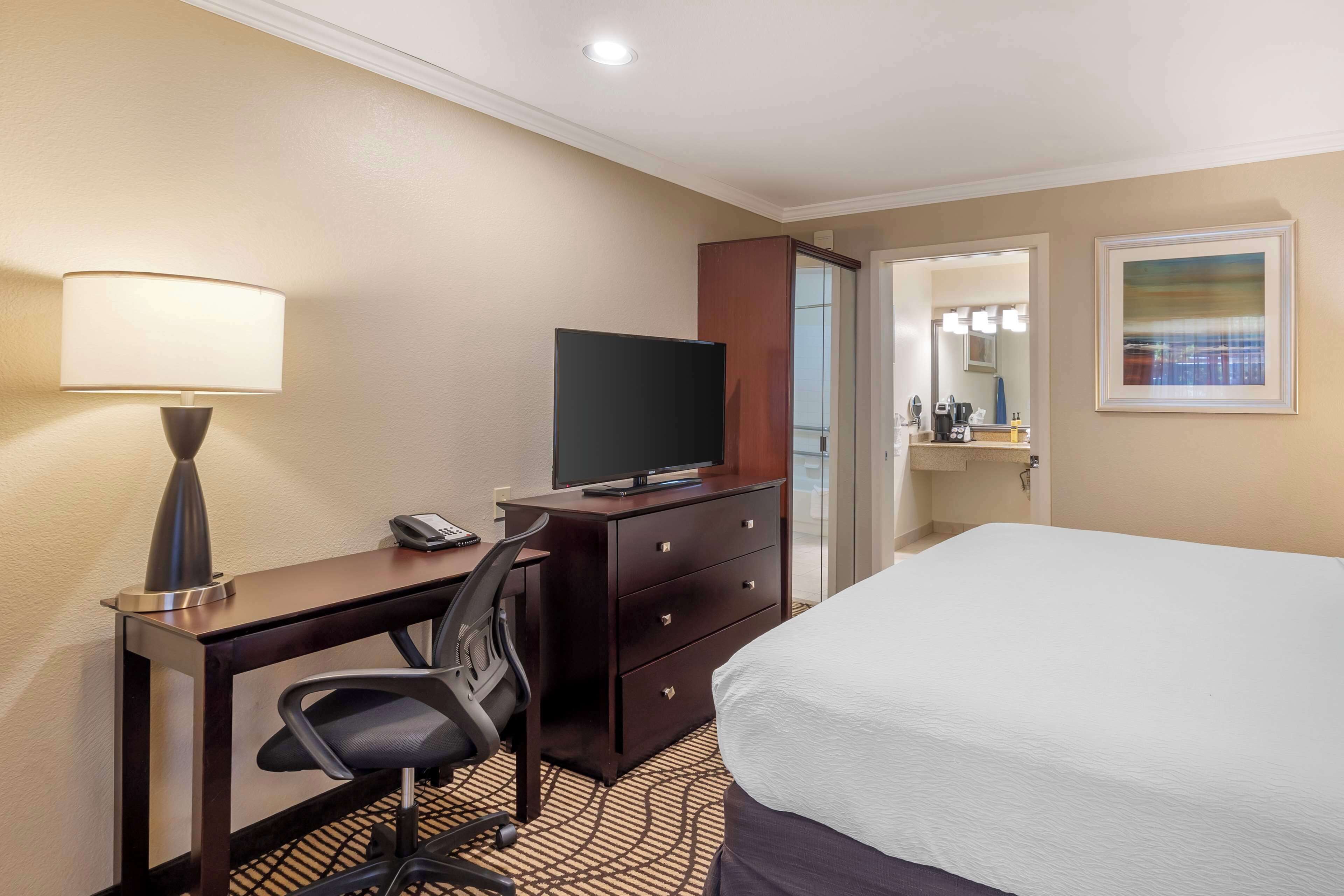 A hotel room with a bed, desk, chair, television, and a bathroom visible through an open door.