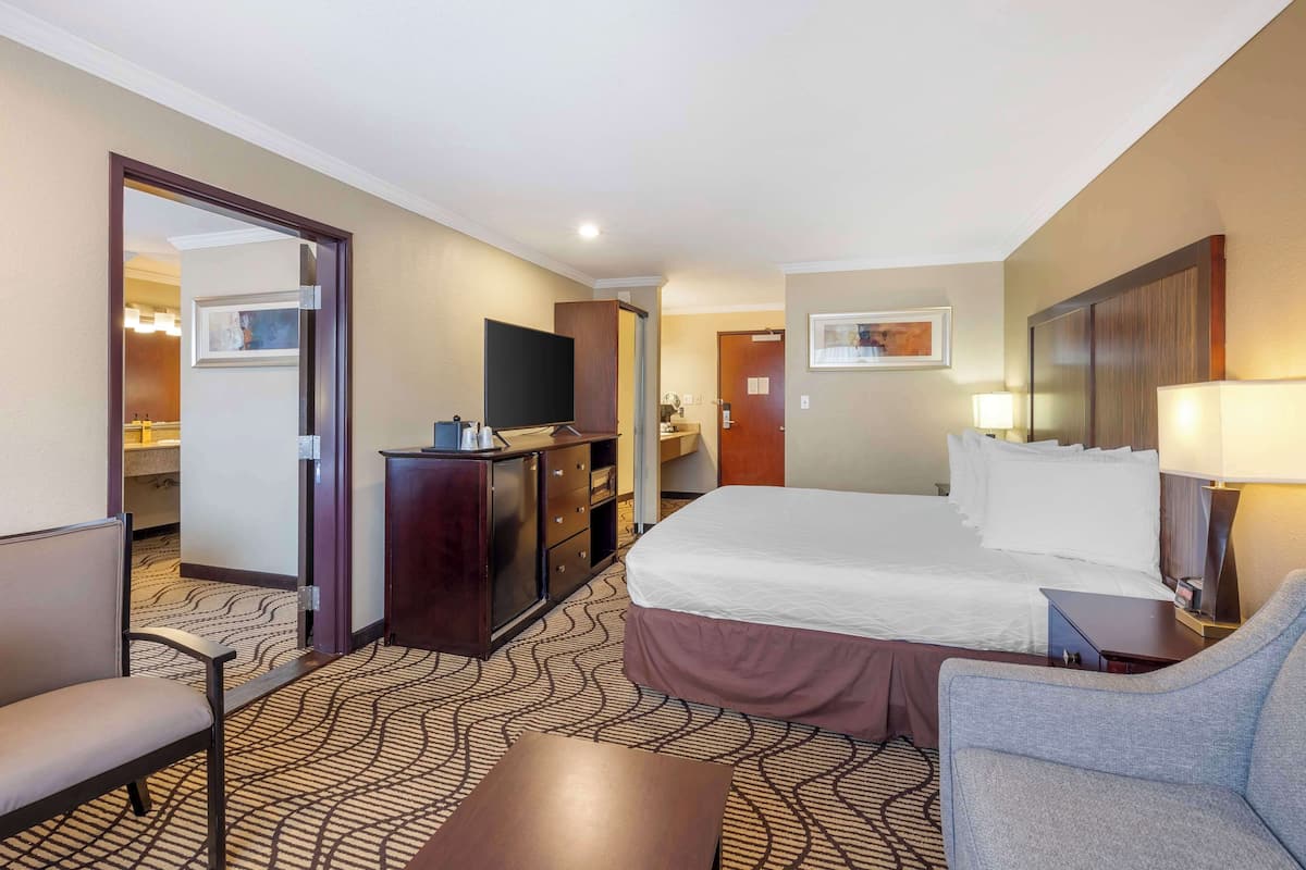 A hotel room with a large bed, a desk, a chair, a television, and a wardrobe.