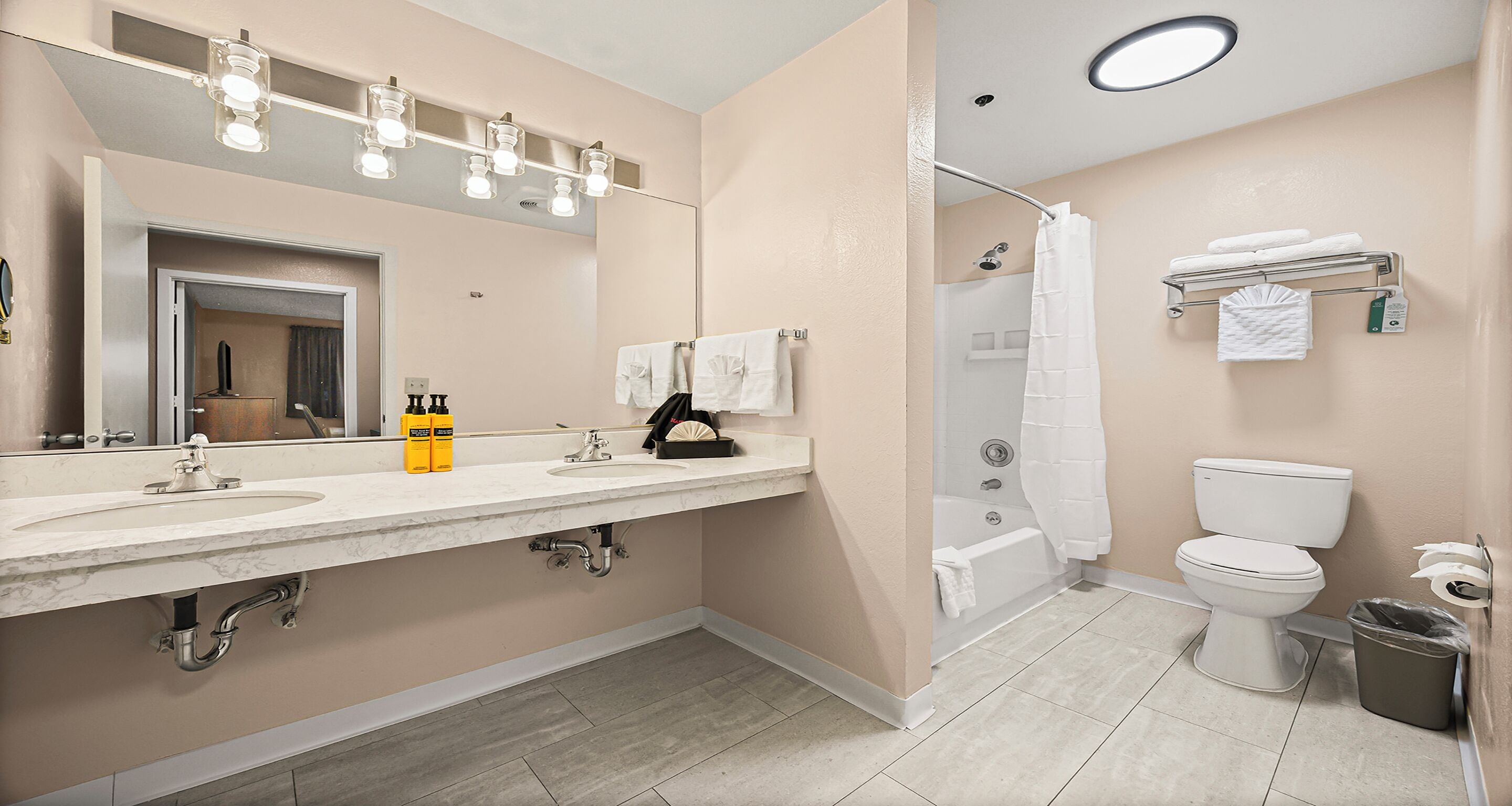 Un baño moderno con lavamanos de mármol, un espejo grande, ducha e inodoro.