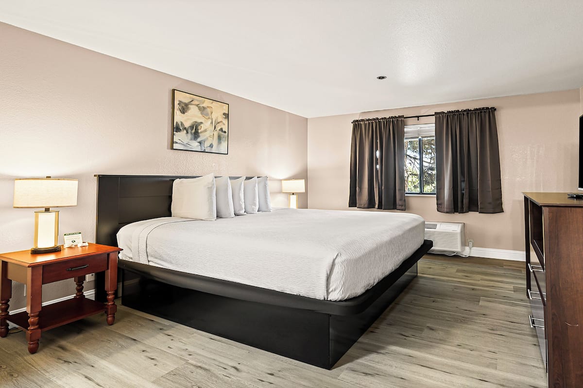 A hotel room with a bed, bedside tables, a TV, and a window with curtains.
