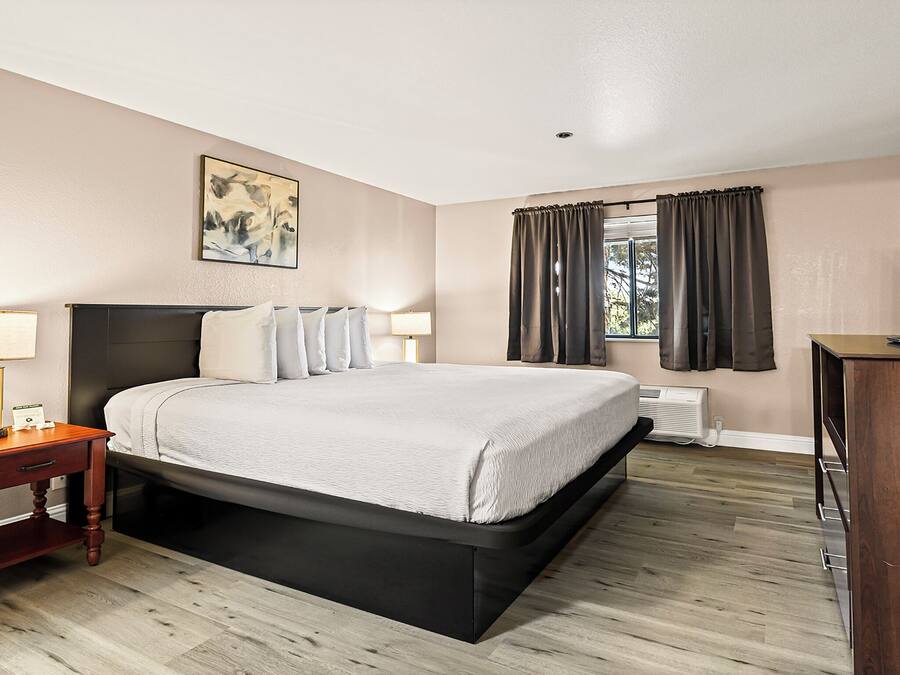 A hotel room with a bed, bedside tables, a TV, and a window with curtains.