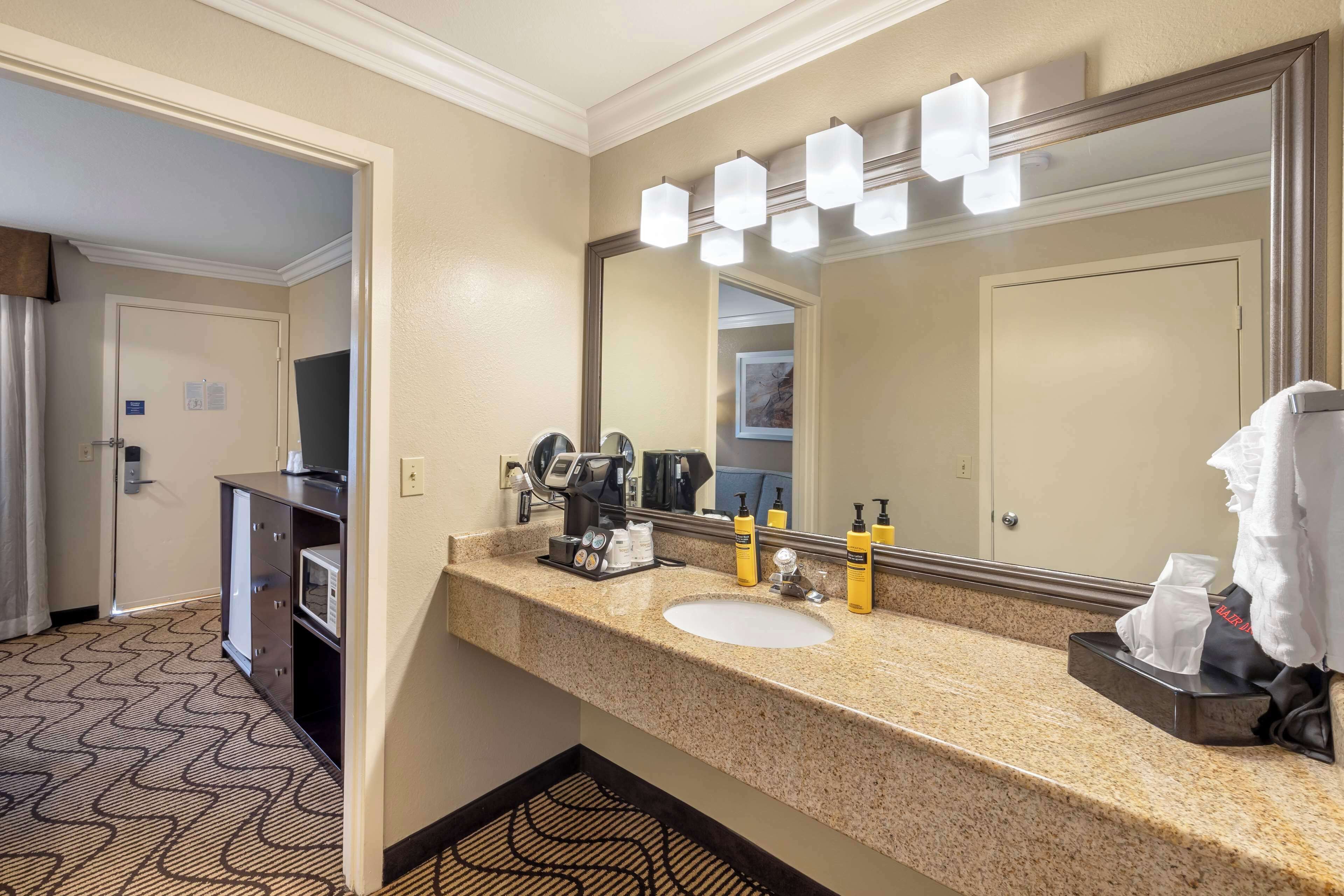 A hotel bathroom with a large mirror, a sink, and a vanity with toiletries.