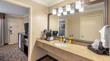 Un baño de hotel con un espejo grande, un lavabo y un mueble de tocador con artículos de aseo.