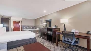 Una habitación de hotel con cama, escritorio, silla, lámpara y espejo.