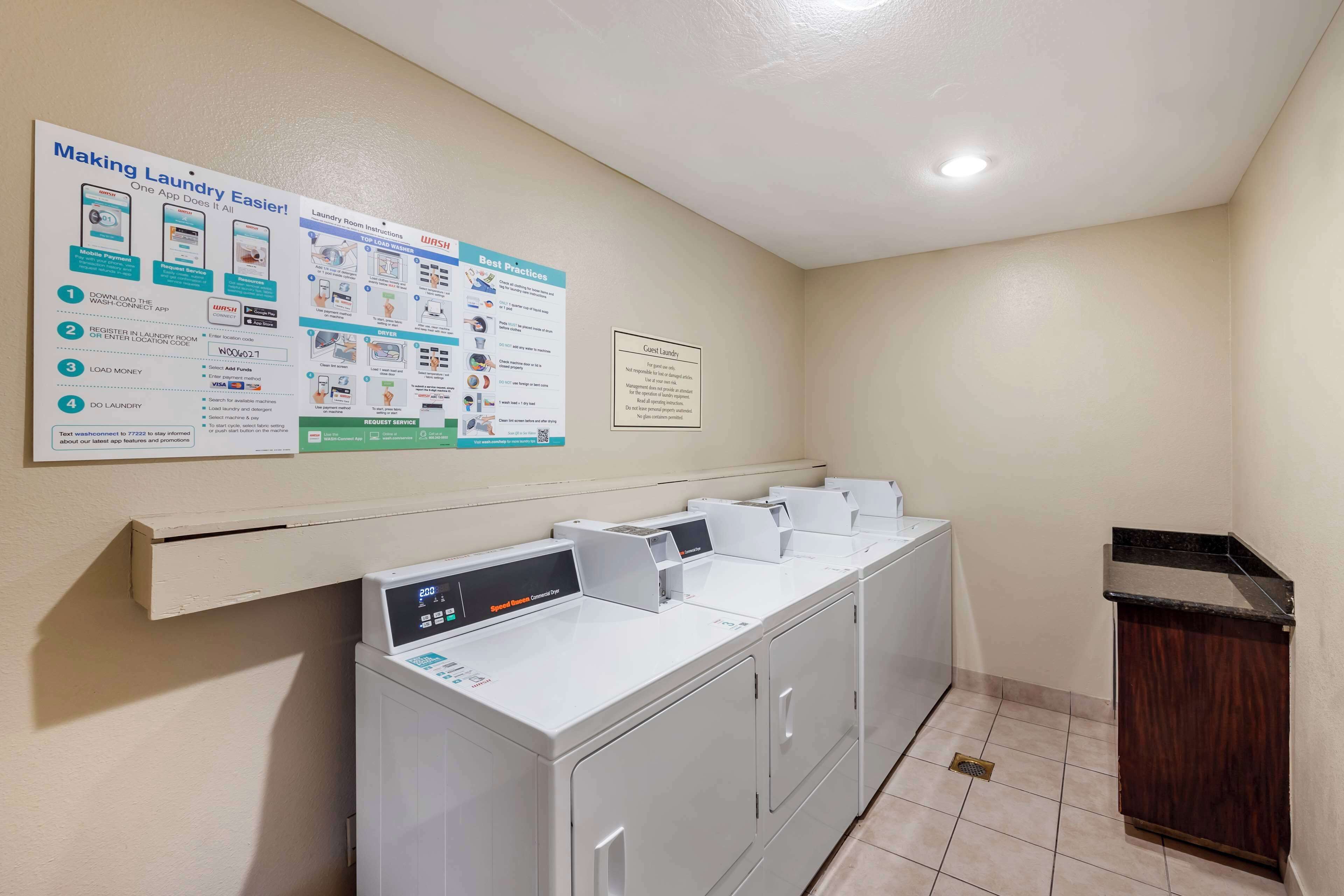Une laverie avec des instructions affichées sur le mur, une rangée de machines à laver et une poubelle.