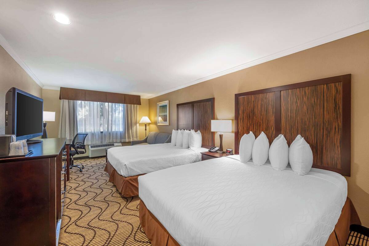 A hotel room with two beds, a desk with a television, a chair, and a desk lamp.