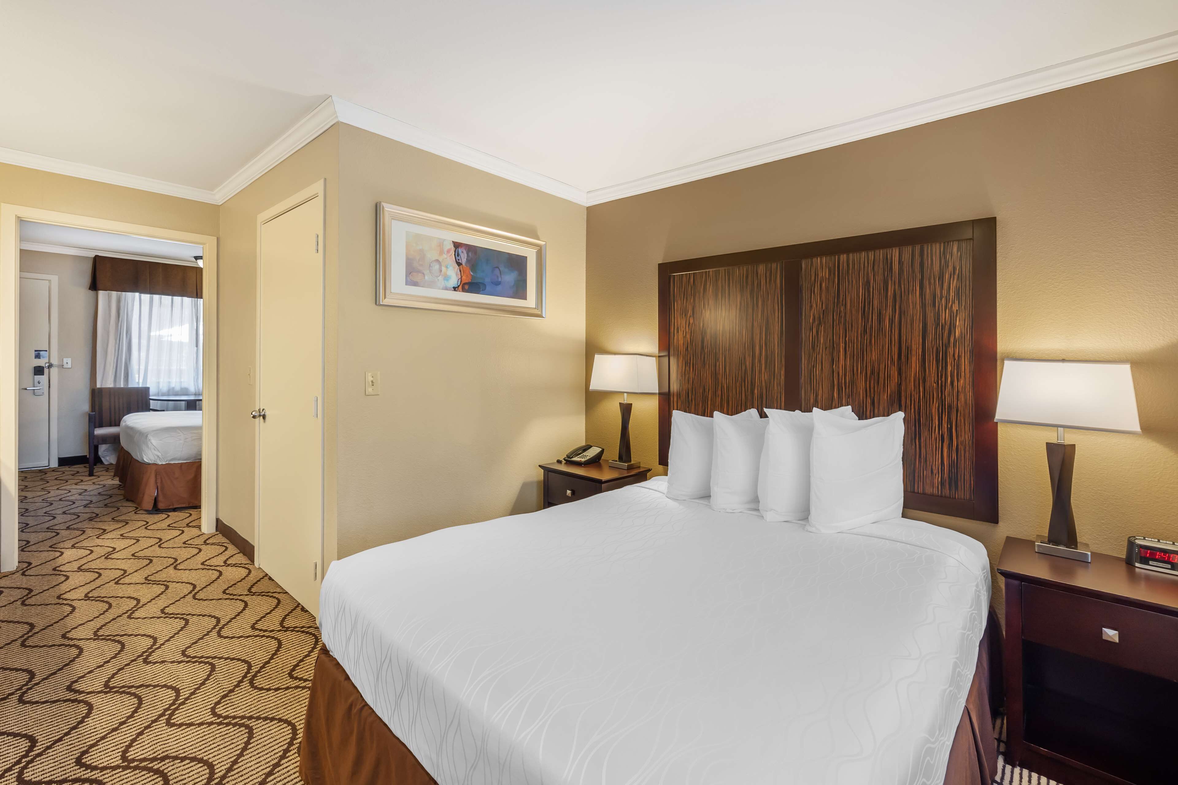 A hotel room with a large bed, two bedside tables with lamps, a painting on the wall, and a carpeted floor.