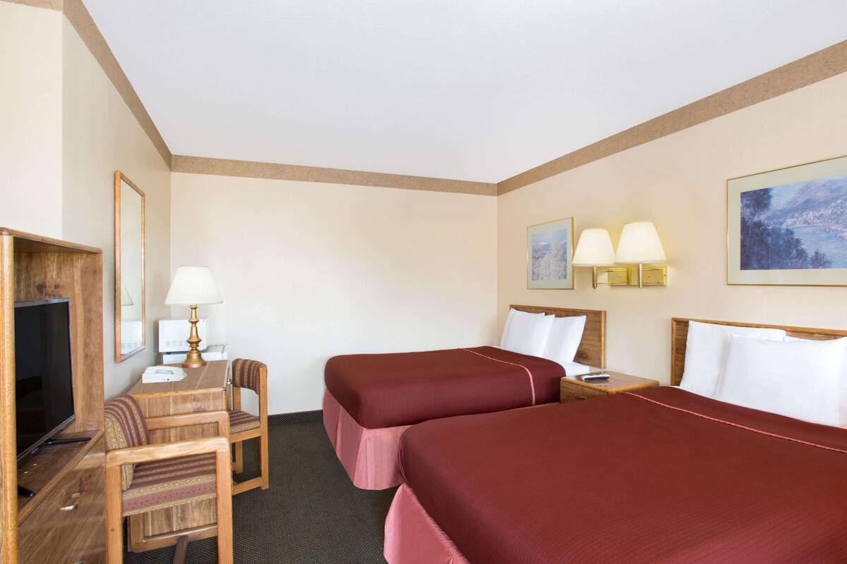 Een hotelkamer met twee bedden, een bureau met stoel, een televisietoestel en twee wandlampen.