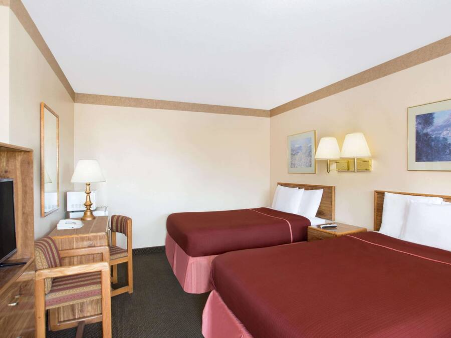 A hotel room with two beds, a desk with a chair, a television, and two wall-mounted lamps.