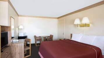 A hotel room with a bed, a desk with a TV, a chair, and two wall-mounted lamps.