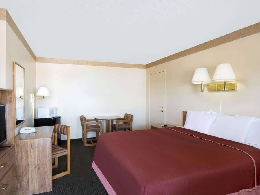 A hotel room with a bed, a desk with a TV, a chair, and two wall-mounted lamps.