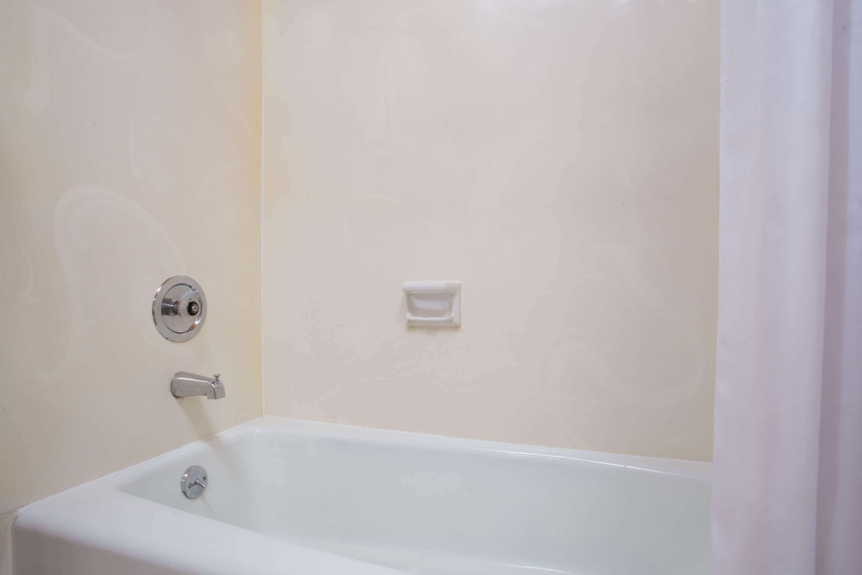 A white bathtub with a chrome faucet and a soap dish on the wall.