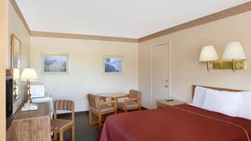 Une chambre d’hôtel avec un grand lit, un bureau avec une lampe, deux chaises, une petite table et deux lampes fixées au mur.
