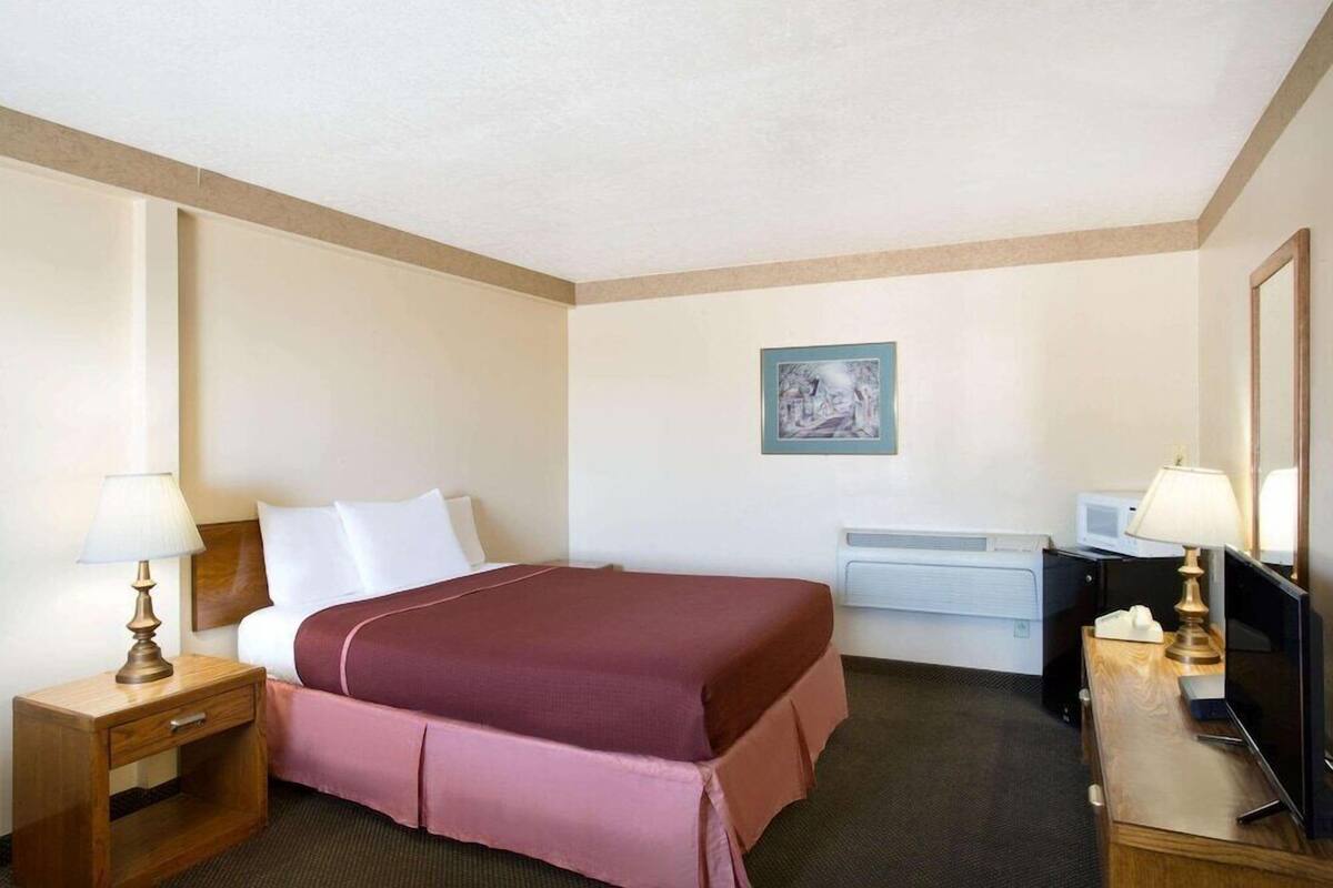 Een hotelkamer met een bed, een bureau met een computer, een televisie en een wandairconditioning.