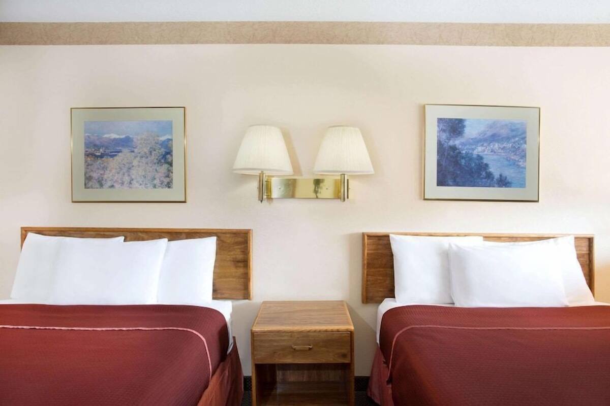 Een hotelkamer met twee bedden, een houten nachtkastje en twee wandlampen.
