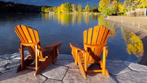 Two wooden Adirondack chairs facing a calm lake with a dock and trees in the background. - Deerhurst Resort (Huntsville)