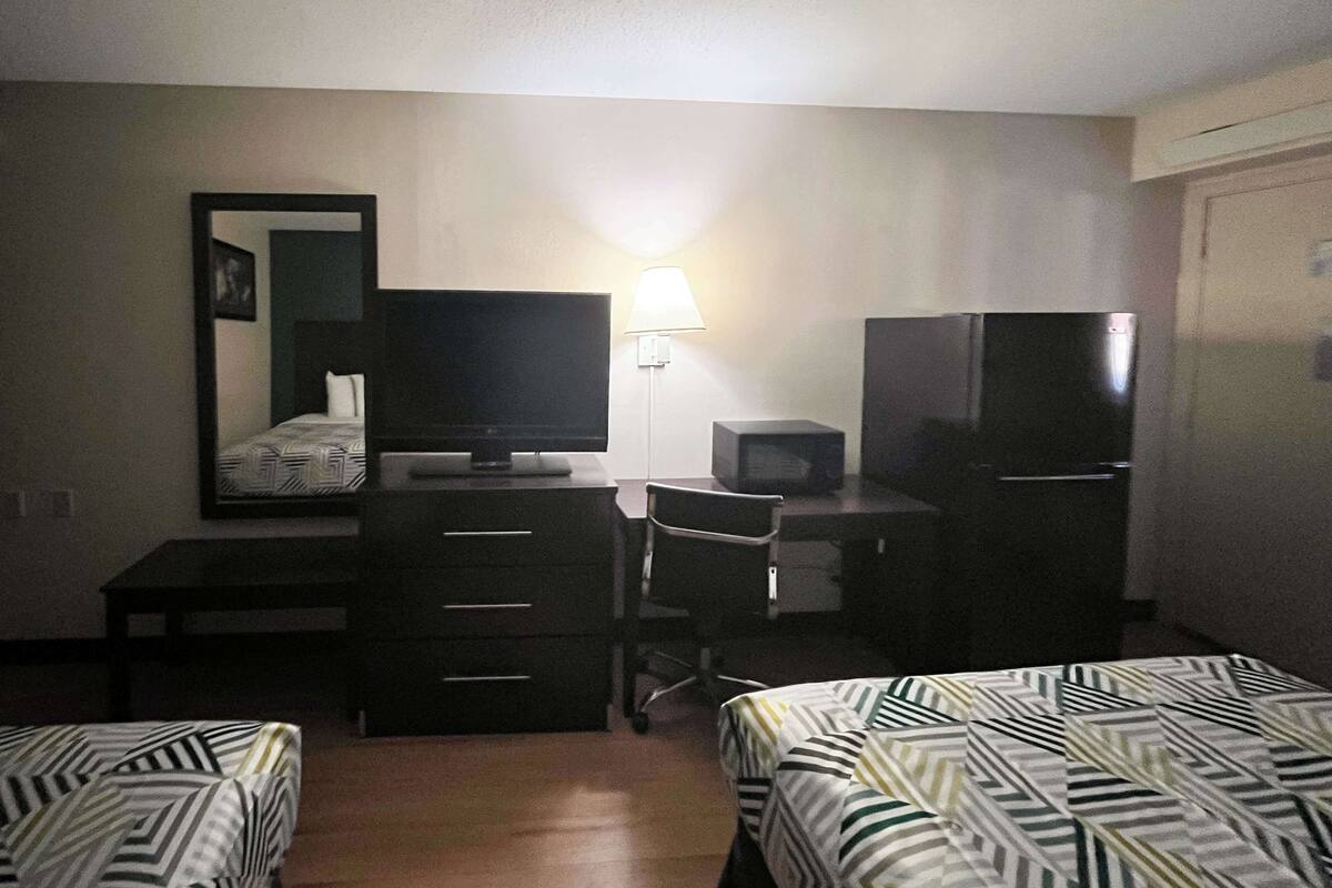 A hotel room with two beds, a desk with a computer and a TV, a lamp, and a refrigerator.