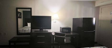 A hotel room with two beds, a desk with a computer and a TV, a lamp, and a refrigerator.