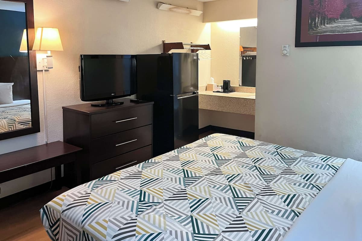 A hotel room with a bed, a TV, a refrigerator, a small desk, and a mirror.