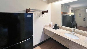 A hotel bathroom with a black refrigerator, a sink, a mirror, and a towel rack.