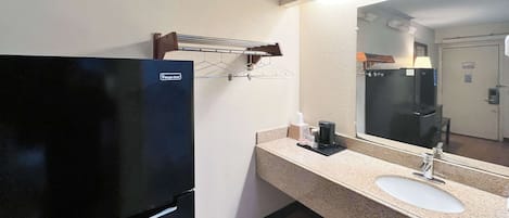 A hotel bathroom with a black refrigerator, a sink, a mirror, and a towel rack.