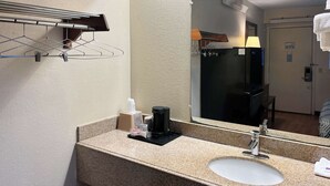 A hotel bathroom with a granite countertop, a white sink, a towel dispenser, a coffee maker, and a towel rack.