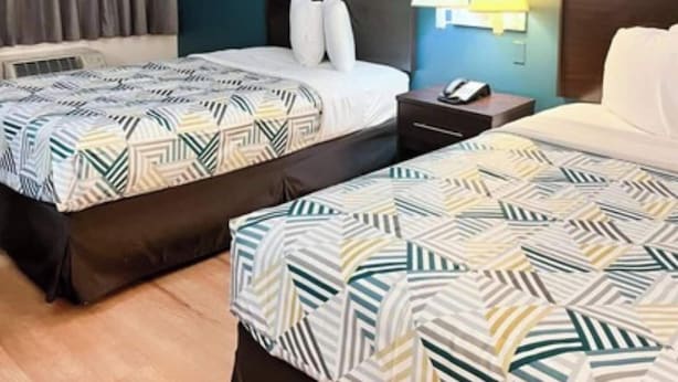 A hotel room with two beds, a nightstand, a lamp, and a telephone.