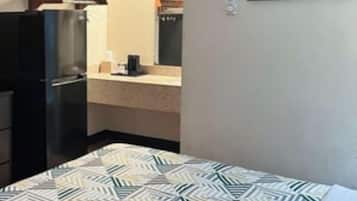 A hotel room with a bed, a kitchenette, and a framed picture on the wall.
