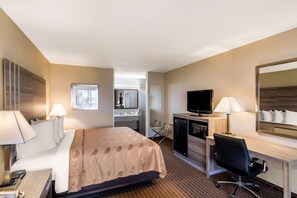 A hotel room with a bed, desk, TV, and a kitchenette.