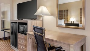 Habitación de hotel con televisión de pantalla plana, microondas, refrigerador, escritorio con silla, lámpara y espejo grande.