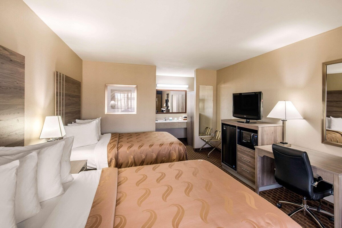 Habitación de hotel con dos camas, un escritorio, televisor, espejo y kitchenette.