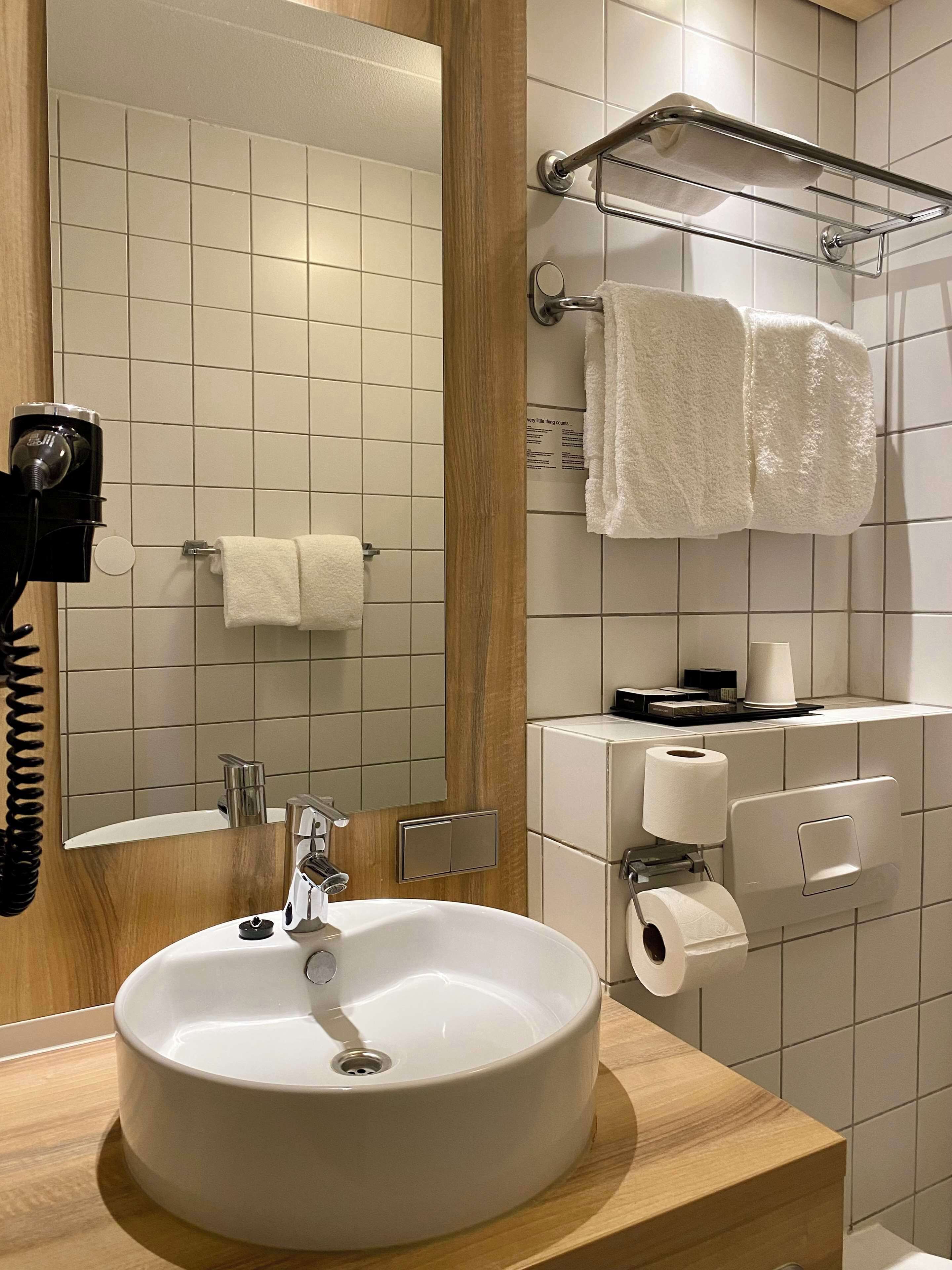 Une salle de bain moderne avec un lavabo rond, un miroir, un porte-serviettes et un distributeur de papier toilette.