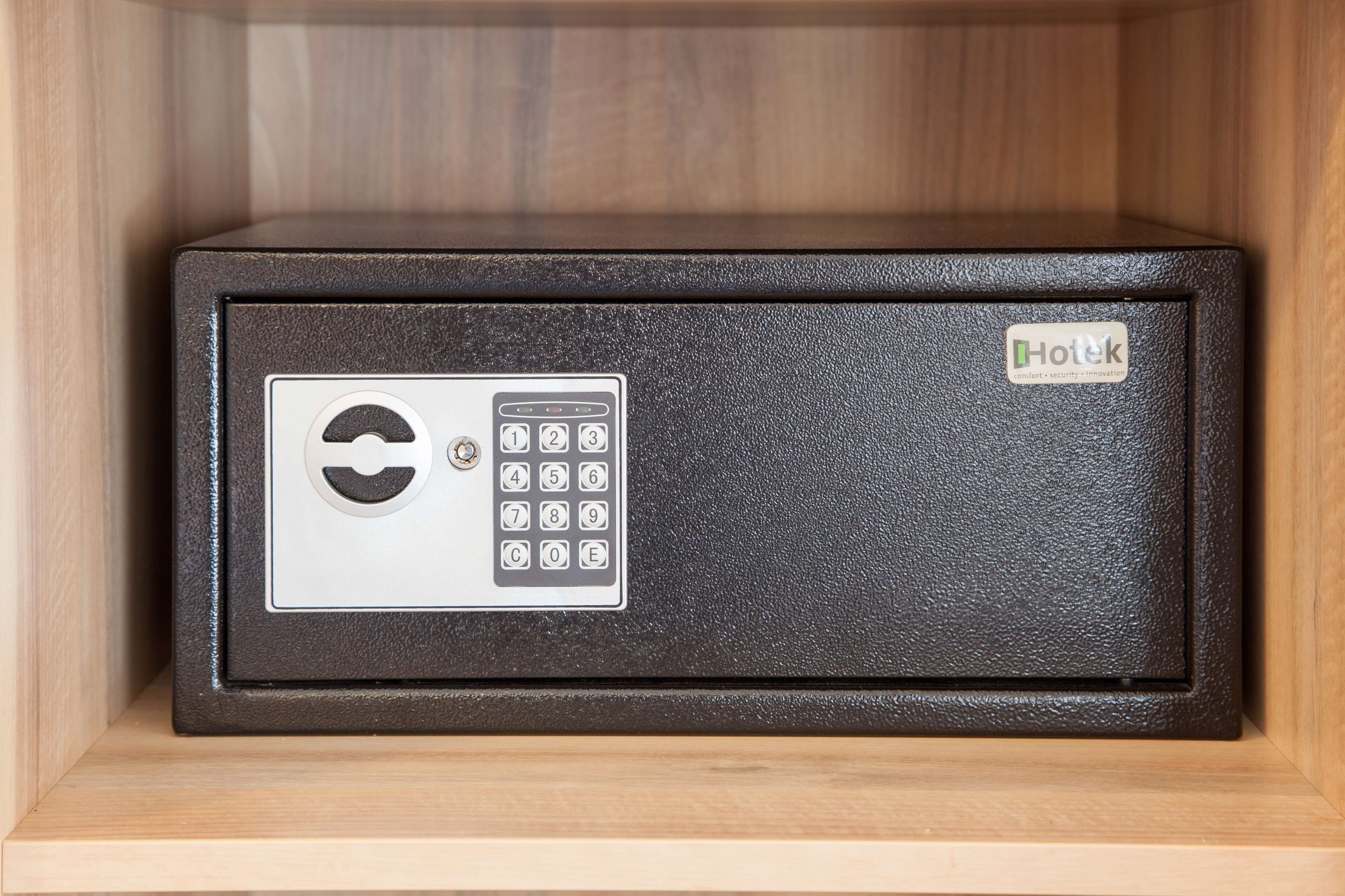 A secure, metallic safe with a keypad and a lock mechanism, placed inside a wooden cabinet.