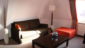 A modern living room with a sofa, a coffee table, a lamp, and a window with curtains. - Best Western Hotel Baars (Harderwijk)
