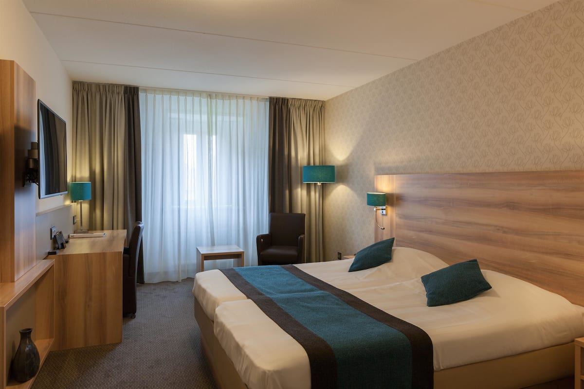 Una habitación de hotel con una cama grande, un escritorio, una silla, un televisor y una lámpara.
