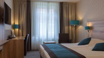 Una habitación de hotel con cama, escritorio, silla, lámparas y televisor.