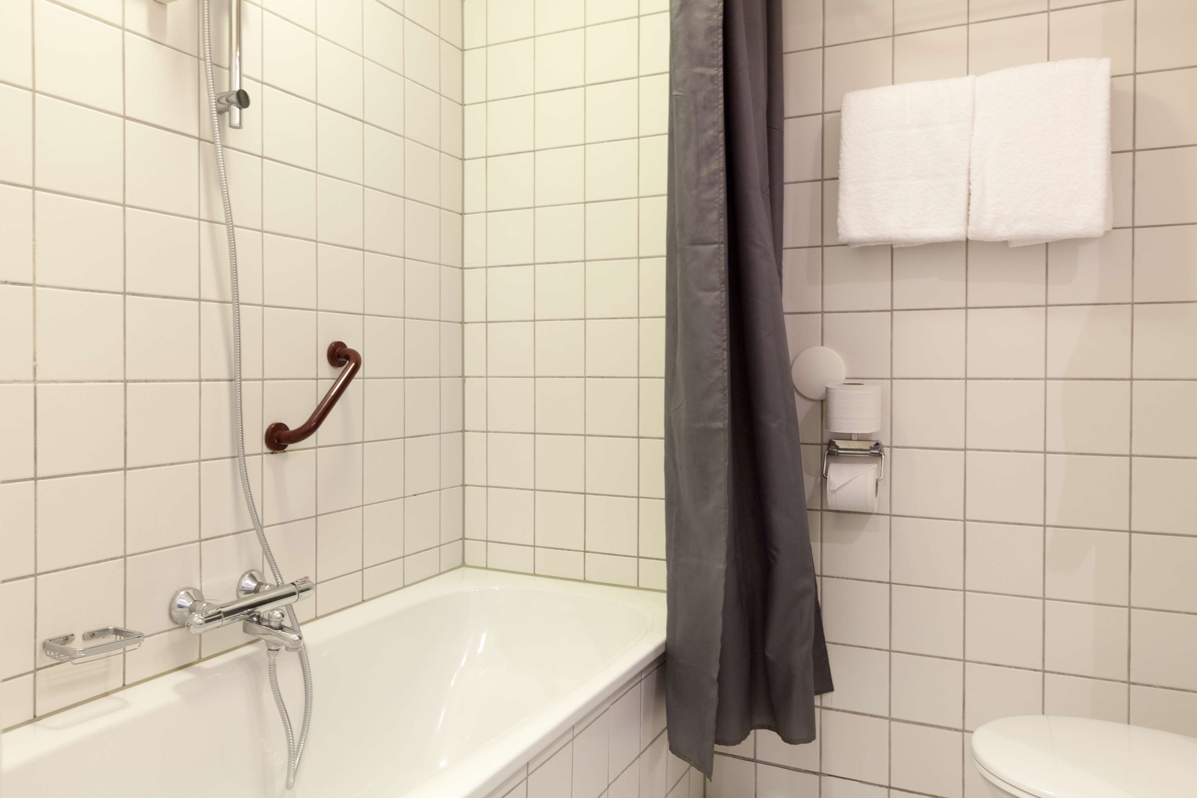 A bathroom with a white bathtub, a shower with a handheld showerhead, a towel rack with a white towel, and a toilet.